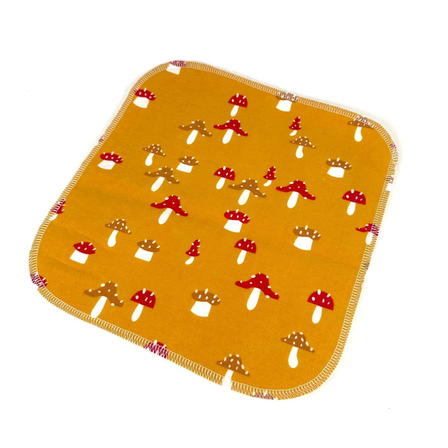 A single Miche Niche flannel napkin in a pattern with mushrooms on a orange buttercream colored background showing the square size, rounded corners, and serged edges