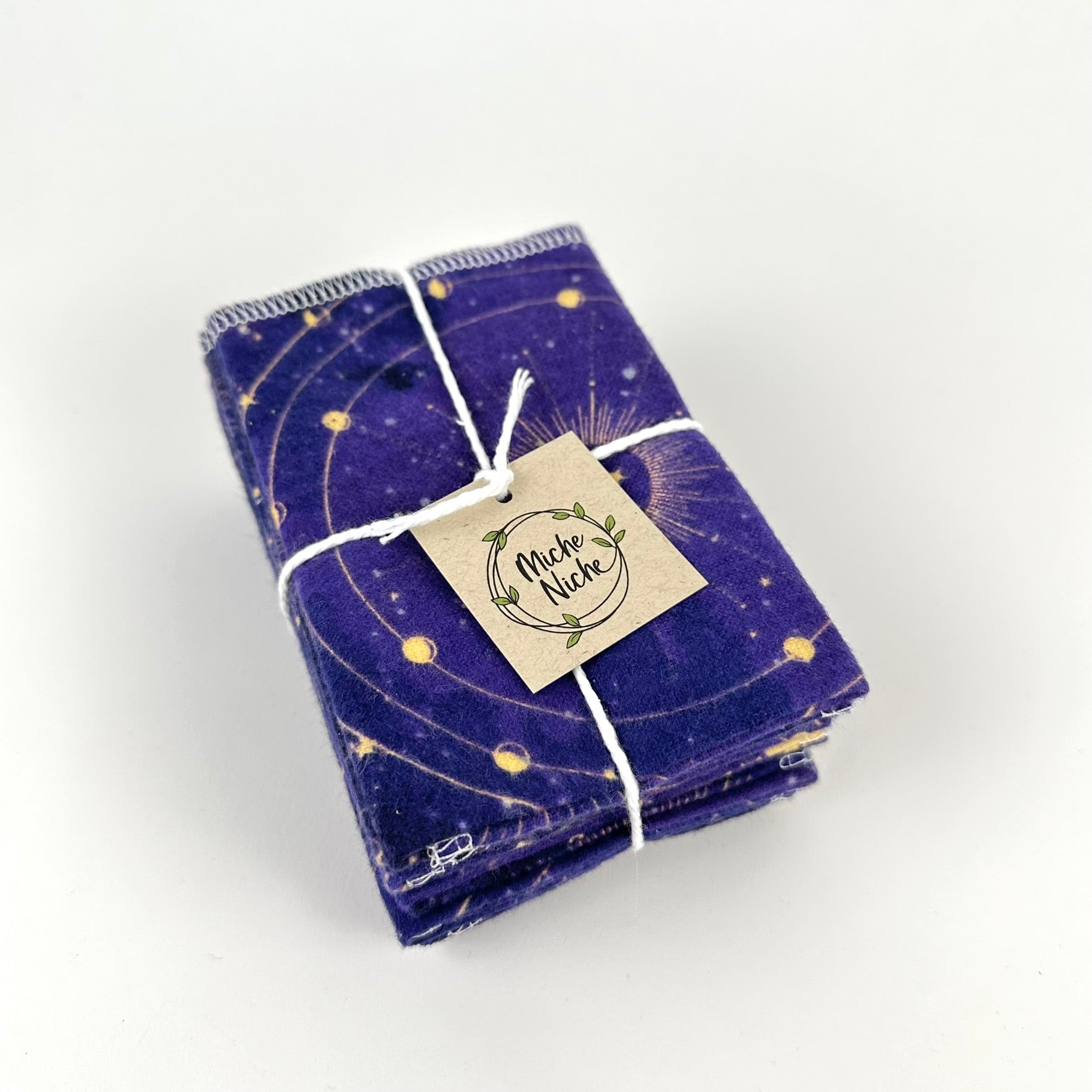 A pack of Miche Niche flannel napkins in a pattern of yellow astrological symbols and stars on a dark blue background