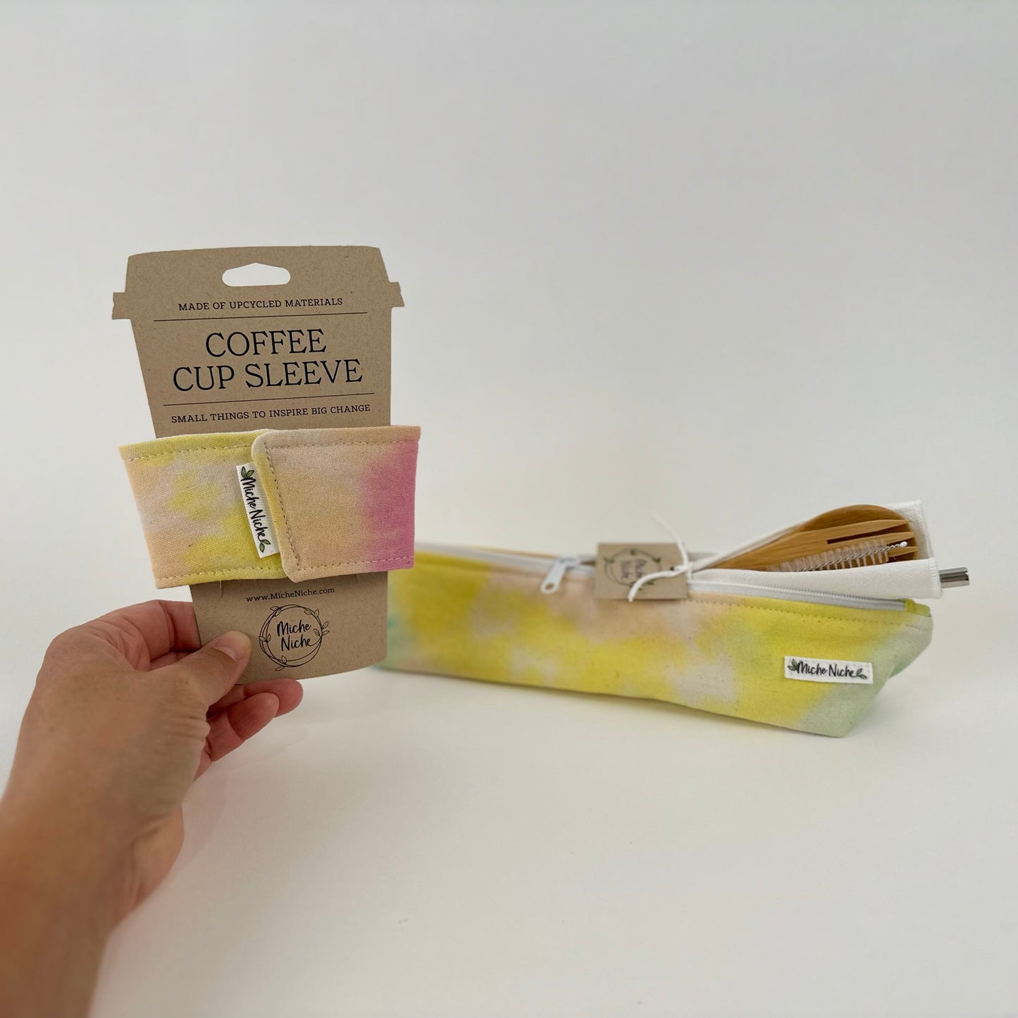 A matching set of a Miche Niche zipper pouch and coffee cup sleeve in a hand dyed pastel yellow, green, and pink tie dye pattern