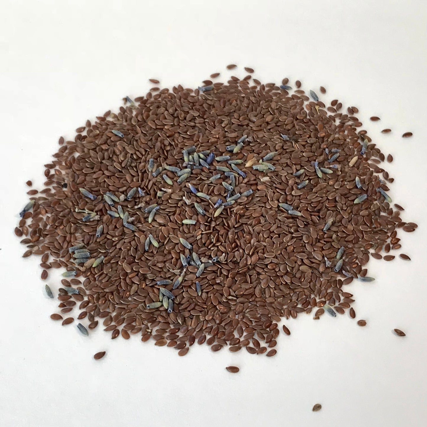 This is a photo of a pile of flax seeds and lavender buds taken on a white background.